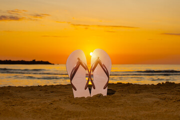 Flip flops stuck in the sand on the beach with the sun in the middle as dawn occurs. vacation concept
