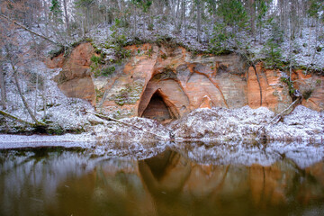 View to the Angels cave, a red sandstone cliff at the river Salaca in Skanaiskalns Nature Park in Mazsalaca in April in Latvia - obrazy, fototapety, plakaty