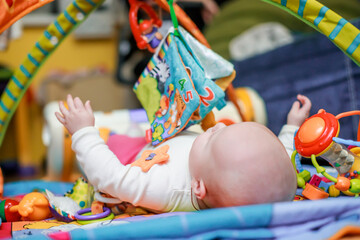 Fototapeta premium The baby lies on a developmental mat and flips through a textile educational book with the image of animals. The child learns about the world and learns shapes and colors while playing.