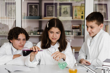 School education. Cheerful classmates in chemistry lesson hold flasks with liquid for experiments. Happy friends study together in class in laboratory.