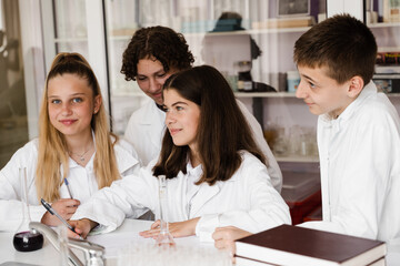 Discussion with a teacher at a chemistry lesson in a laboratory. Group of classmates are discussing chemistry experiments and homework at school. Education concept.