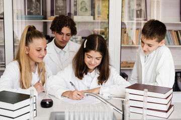 Discussion with a teacher at a chemistry lesson in a laboratory. Group of classmates are discussing chemistry experiments and homework at school. Education concept.