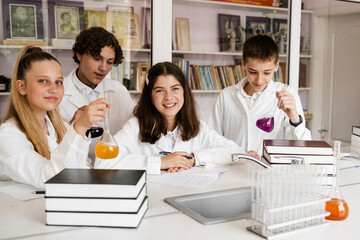 Obraz na płótnie Canvas Schoolchildren studying at chemistry lesson in classrom. Pupils writing in notebook, holding flasks with liquid for experiments and have fun together. School education.