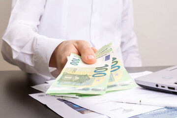 a man's hand holds out one hundred euro bills against the background of an office table with a...