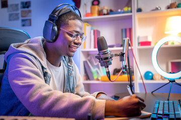 Young smiling man wearing headphones and talking into a microphone at the radio station recording...