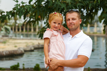 Fototapeta premium Dad holds his daughter in his arms, a walk in the city park, family leisure
