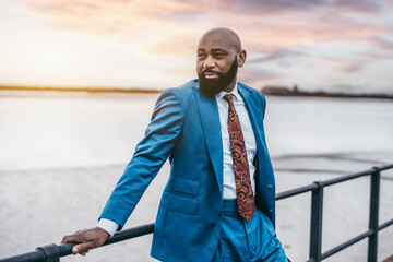 A portrait of a fashionable manly bald bearded black man entrepreneur in a blue tailored suit with...