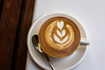 white cup of cappuccino with latte art on white saucer with spoon. beatiful beginning of the day