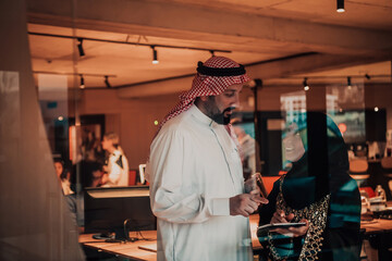 Portrait photo of Arab leader businessman with muslim hijab woman discussing business projects while using tablets and smartphone in modern glass office 