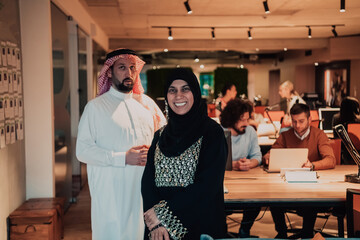 Portrait photo of Arab leader businessman with muslim hijab woman discussing business projects while using tablets and smartphone in modern glass office 