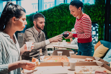 Eating pizza with diverse colleagues in the office, happy multi-ethnic employees having fun together during lunch, enjoying good conversation, and emotions