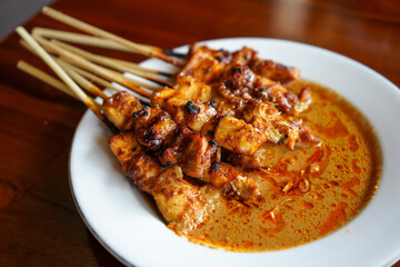 Satay or sate in Indonesian spelling, is a Southeast Asian dish of seasoned, skewered and grilled meat, served with a sauce. The earliest preparations of satay is Javanese cuisine. Brown background.