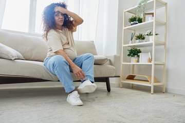 Pregnant woman sitting on sofa at home and putting on pregnancy-friendly shoes with problem due to belly