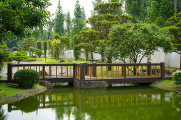Obraz premium Traditional oriental park or garden from Japan or China with fish pond, lake or river, wooden bridge, meadow, and trees. Japanese garden design. Taman Bunga Nusantara, Cianjur, West Java, Indonesia.