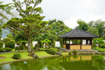 Obraz premium Traditional oriental park or garden from Japan or China with fish pond, lake or river, wooden bridge, meadow, and trees. Japanese garden design. Taman Bunga Nusantara, Cianjur, West Java, Indonesia.