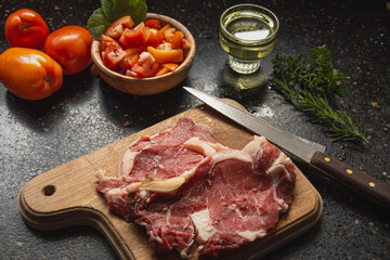 meat on board accompanied by tomato salad, oil, rosemary and parsley