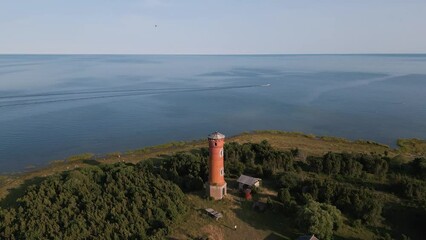 aerial drone flight towards a lost place old lighthouse at the coast of baltic sea - country side of Estonia in Europe - nature helicopter flyover establishing shot summer 2022 - bird view - ship