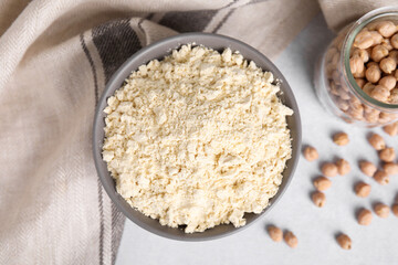 Chickpea flour in bowl and seeds on light grey table, flat lay
