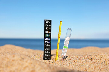 Different weather thermometers in sand near sea