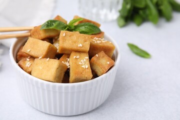 Bowl with delicious fried tofu, basil and sesame seeds on white table, closeup