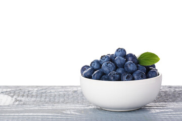 Tasty fresh blueberries and green leaves in bowl on grey wooden table against white background