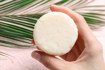 Woman holding solid shampoo bar at pink table, closeup. Hair care