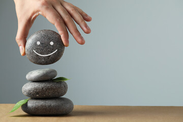 Woman putting stone drawn happy face onto stack against grey background, closeup and space for...