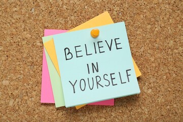 Notes with phrase Believe In Yourself pinned on corkboard, top view. Motivational quote