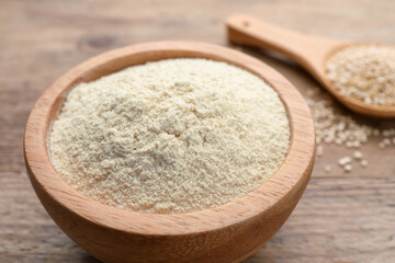 Quinoa flour in bowl and spoon with seeds on wooden table, closeup
