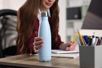 Woman holding thermos bottle at workplace, closeup