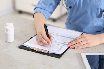 Doctor filling patient's medical card at table in clinic, closeup