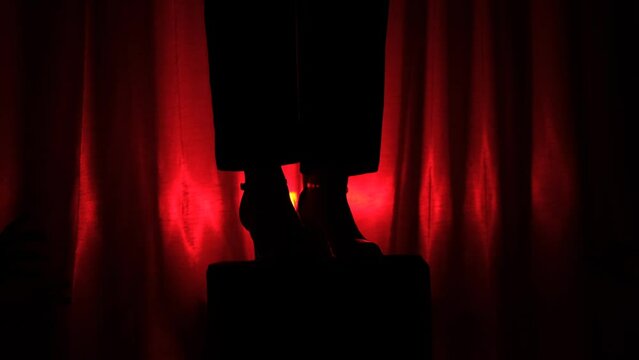 silhouettes of Multiple hands trying to reach legs of actor on the stage on a red dark background. Worship concept, idolize person, idol on the stage