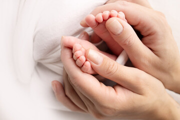 Mother is doing massage on her baby foot. Close up baby feet in mother hands on a white background. Prevention of flat feet, development, muscle tone, dysplasia. Family, love, care, and health concept