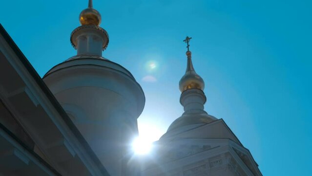 Golden domes with crosses of the Russian Orthodox Church against the backdrop of blue sky and bright sun, giving beautiful flares. Shot in motion