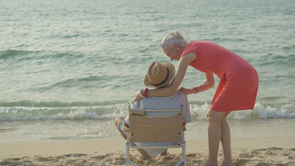 An elderly couple hugs their shoulders at the beach on their summer vacation and they smile and enjoy their vacation.