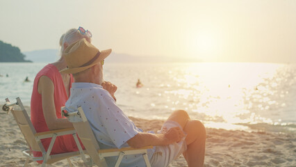 Two elderly men and women sit chair at the beach talking and watching the sun and the sea on their...