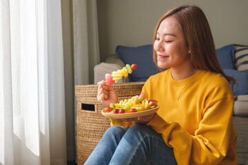 Portrait image of a young woman holding and eating a fresh mixed fruits on skewers