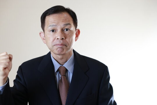 Middle-aged Japanese male businessman wearing navy blue suit on white background holding tablet PC. Conceptual image of a project proposal, strategic business success and negotiation closing.
