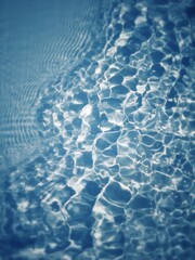 Defocus blurred transparent blue colored clear calm water surface texture with splashes and bubbles. Trendy abstract nature background. Water waves in sunlight with copy space. Blue watercolor shining