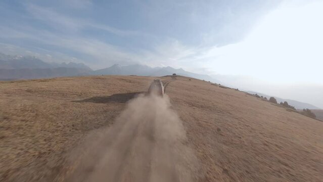 FPV sports drone follow shot SUV red automobile race rally offroad riding desert mountain adventure sand splash. Aerial view cinematic hilly valley dirt road transportation extreme tourism exploration