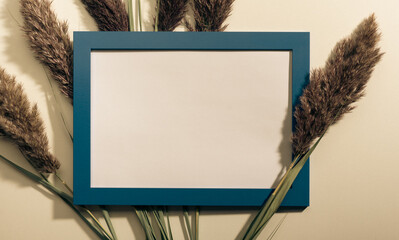 Mockup with blank photo frame and dried pampas grass over beige pastel background with trendy...
