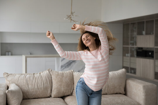 Overjoyed woman dance, jump, moves to favourite music enjoy leisure at home, being active in modern house on carefree weekend. Female celebrate, having festive mood, fooling around indoors. Fun, hobby