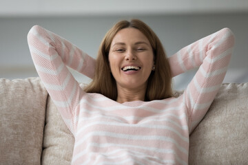 Happy beautiful woman in casual sweater resting leaned on sofa cushions with hands behind head, smile look at camera feels peaceful, enjoy carefree weekend leisure, breathe fresh air relaxing at home