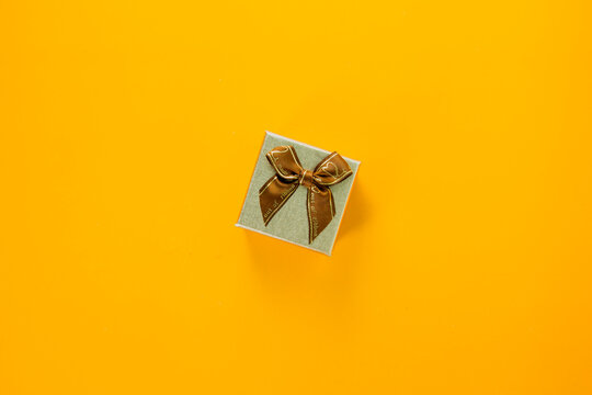 Mini golden gift box with ribbon on yellow background, giving special gift box for Merry New Year and Merry Christmas 2023 concept, yellow gift box on top view.