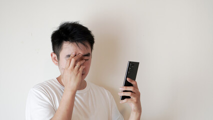a man is expressing upset and distressed after receiving and reading a bad massage or information shown on a phone he was holding over a white background 