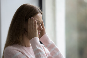 Close up young woman standing indoors suffers from strong headache, chronic migraine, high blood...