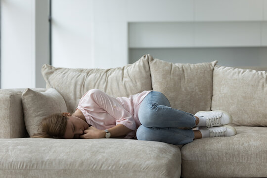 Sad crying woman lying on sofa at home, suffering from mental psychological disorder or depression, troubled with problem, grieving, goes through divorce. Unplanned pregnancy, abortion, miscarriage