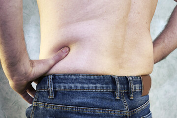 Naklejka premium a man in jeans with a bare torso and a small belly close-up of the concept of overweight body positive