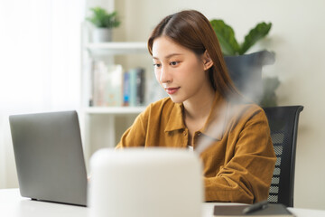Modern air humidifier device during sitting workplace, happy asian young woman using computer work...