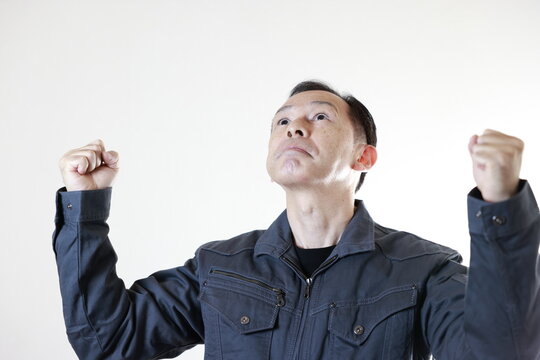 Middle-aged Japanese male worker wearing gray work clothes on white background with hands folded. Concept image of high technology in manufacturing, process work instructions, and working environment.